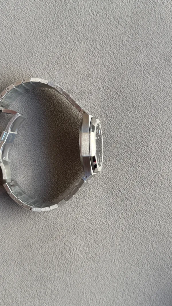 Side view of a silver stainless steel wristwatch with a linked bracelet on a gray textured surface.