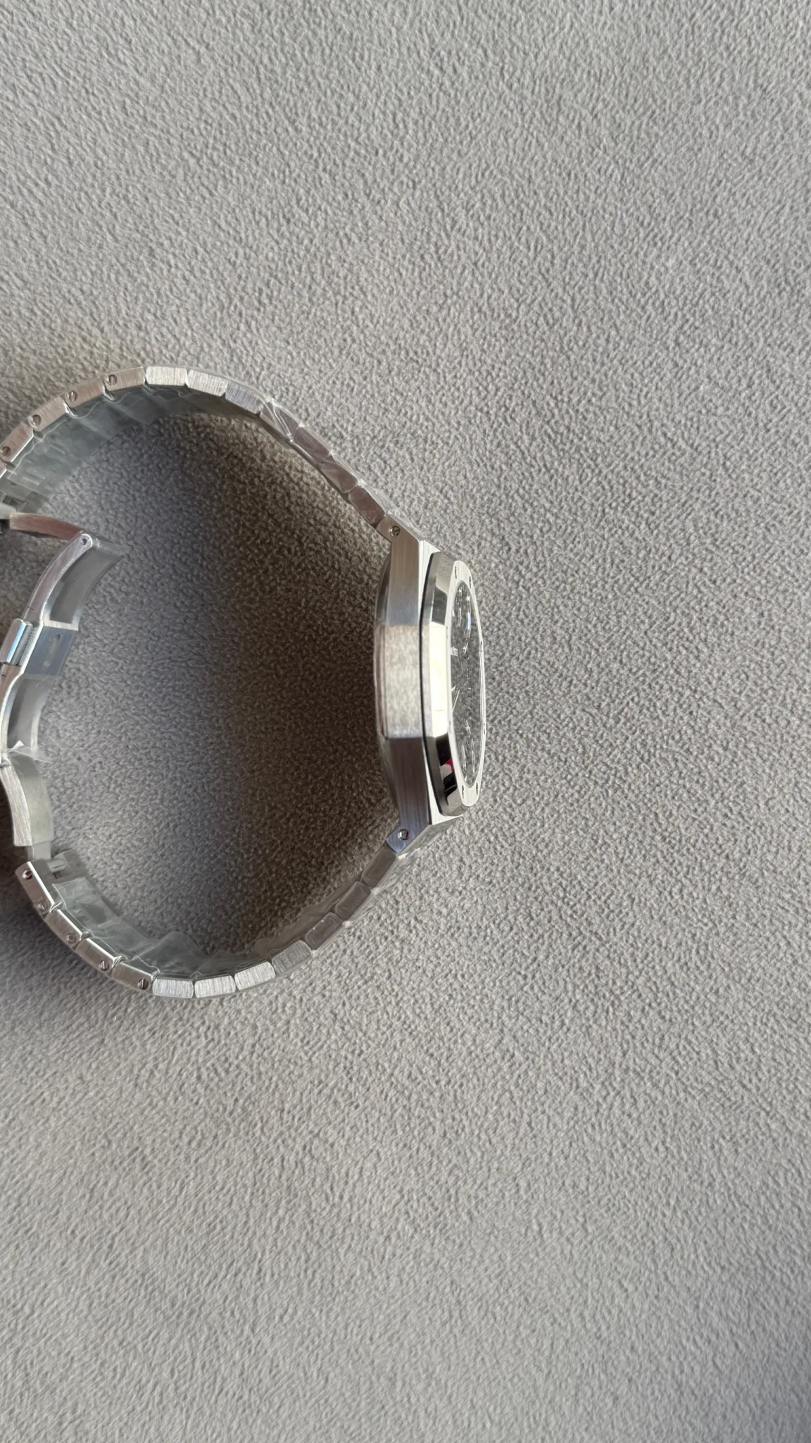 Side view of a silver stainless steel wristwatch with a linked bracelet on a gray textured surface.