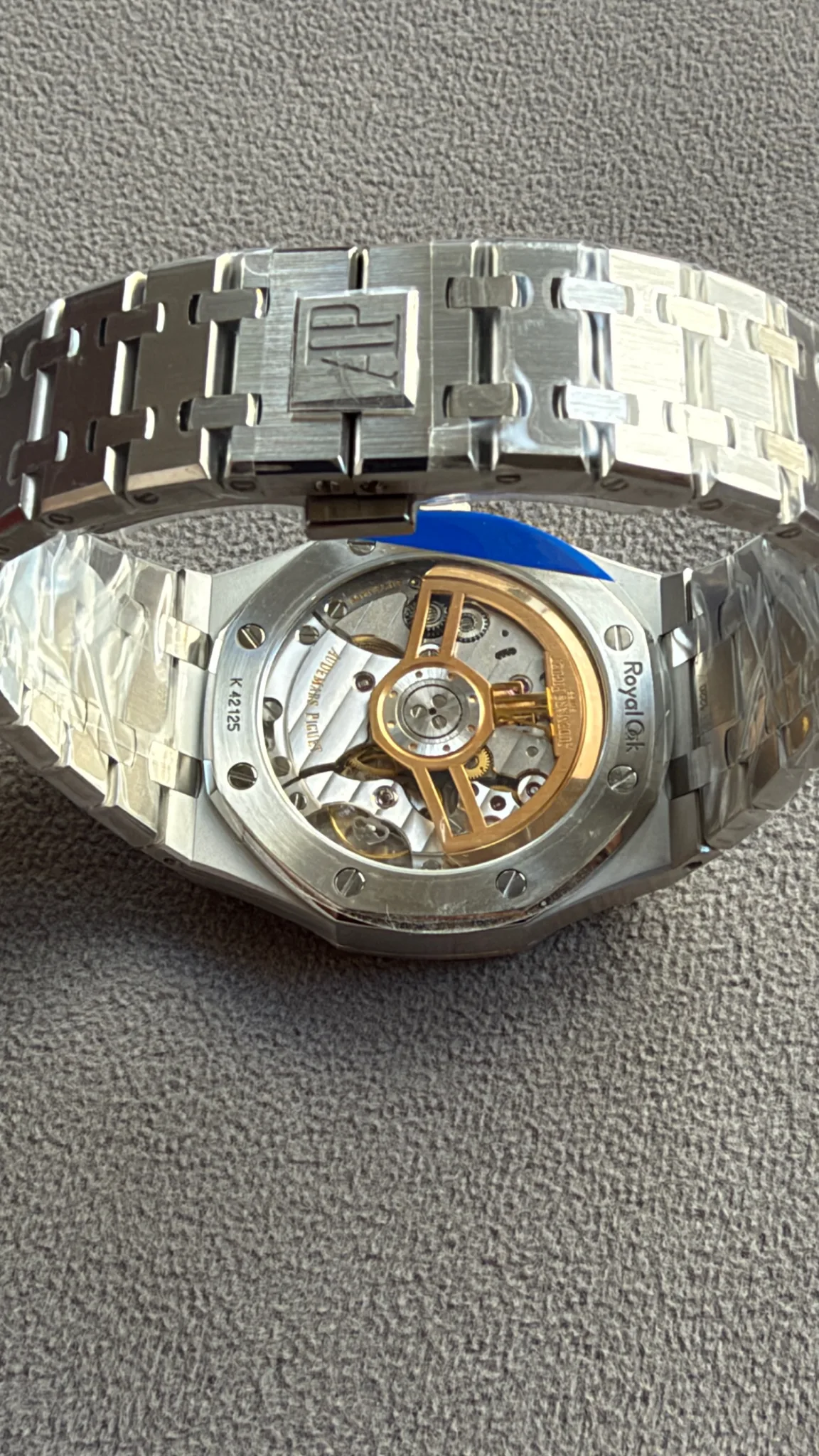 Stainless steel wristwatch with a visible mechanical movement and gold rotor, Royal Oak branding on the back, metal link bracelet visible.