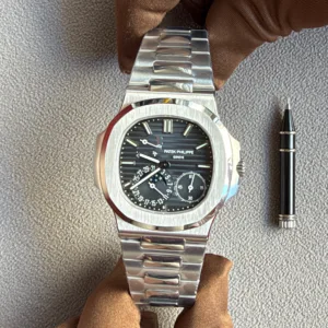 Patek Philippe watch with stainless steel bracelet resting on brown gloves, a pen nearby on a gray fabric surface.