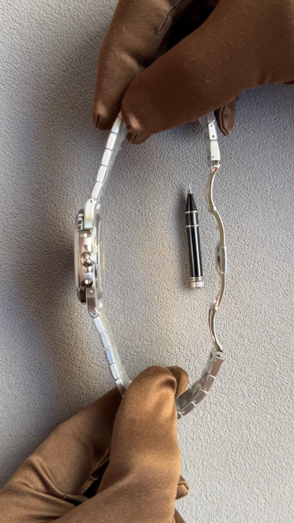 Gloved hand holding a metal watch band with a precision pin tool between links, as if resizing the bracelet.
