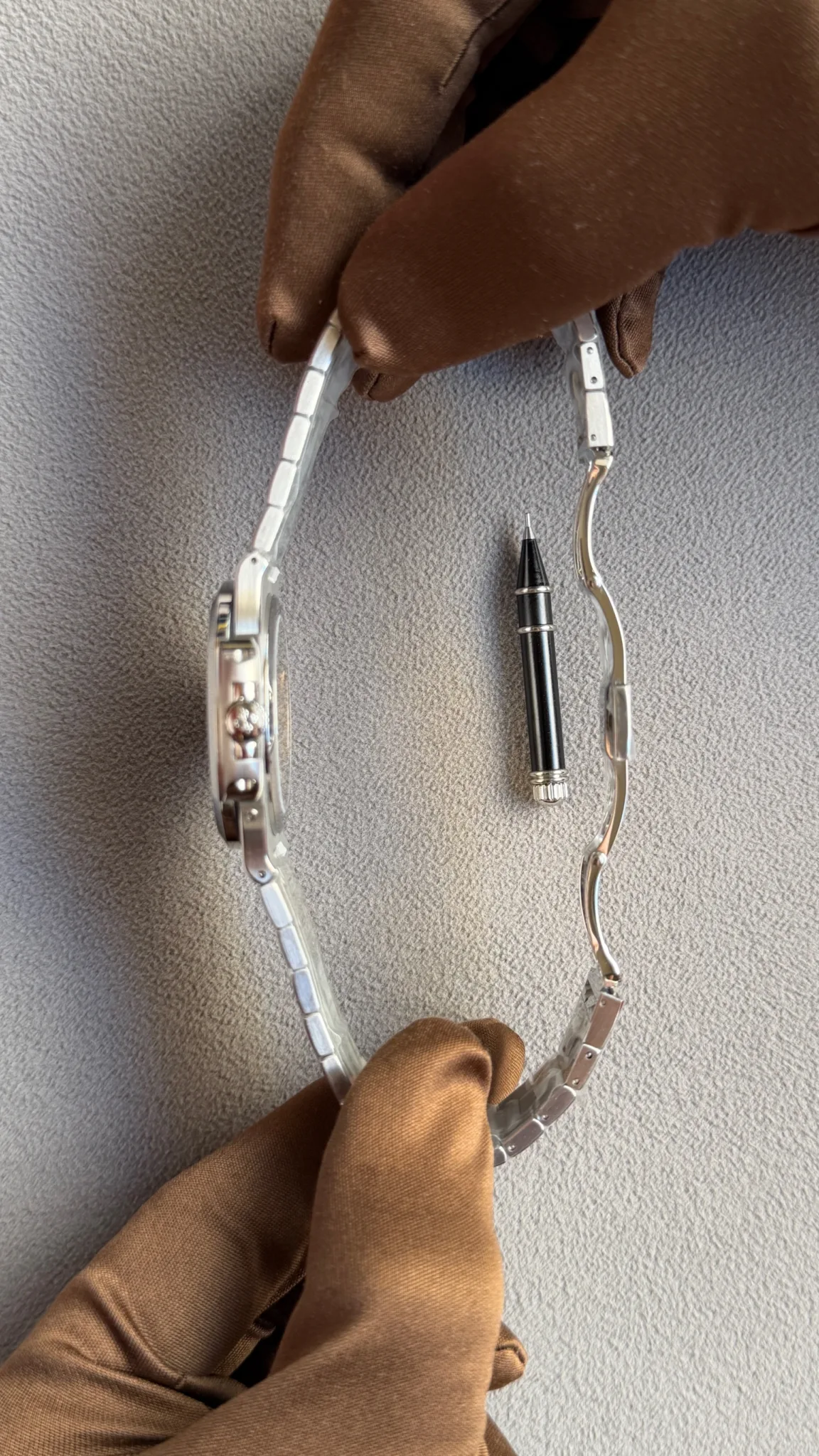 Gloved hand holding a metal watch band with a precision pin tool between links, as if resizing the bracelet.