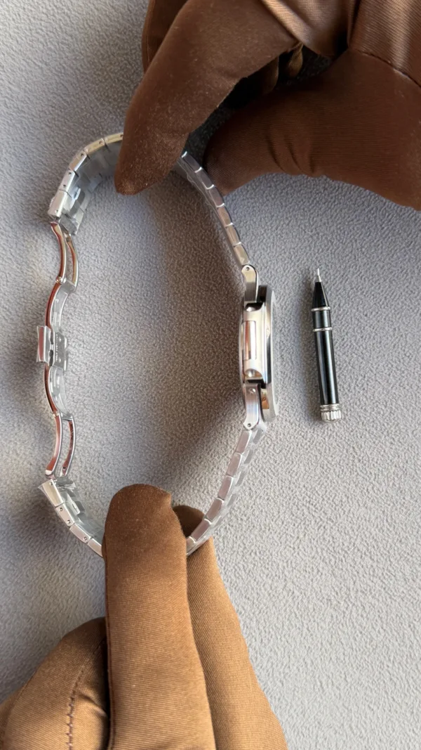 Watch with a metal band and a spring bar tool lying beside it, suggesting watch band work or repair.