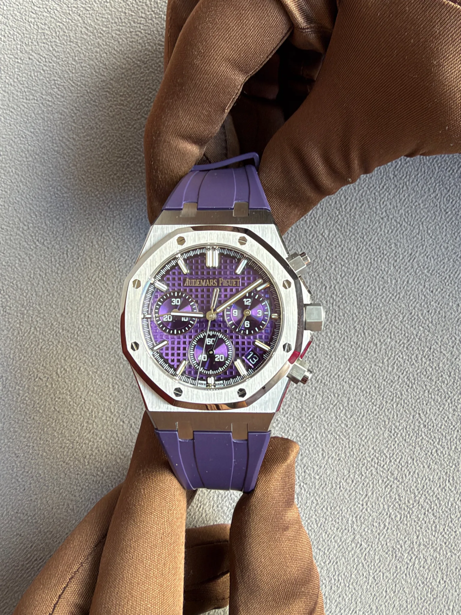 Purple-dial Audemars Piguet Royal Oak watch with a stainless steel case and purple strap resting on a brown fabric surface.