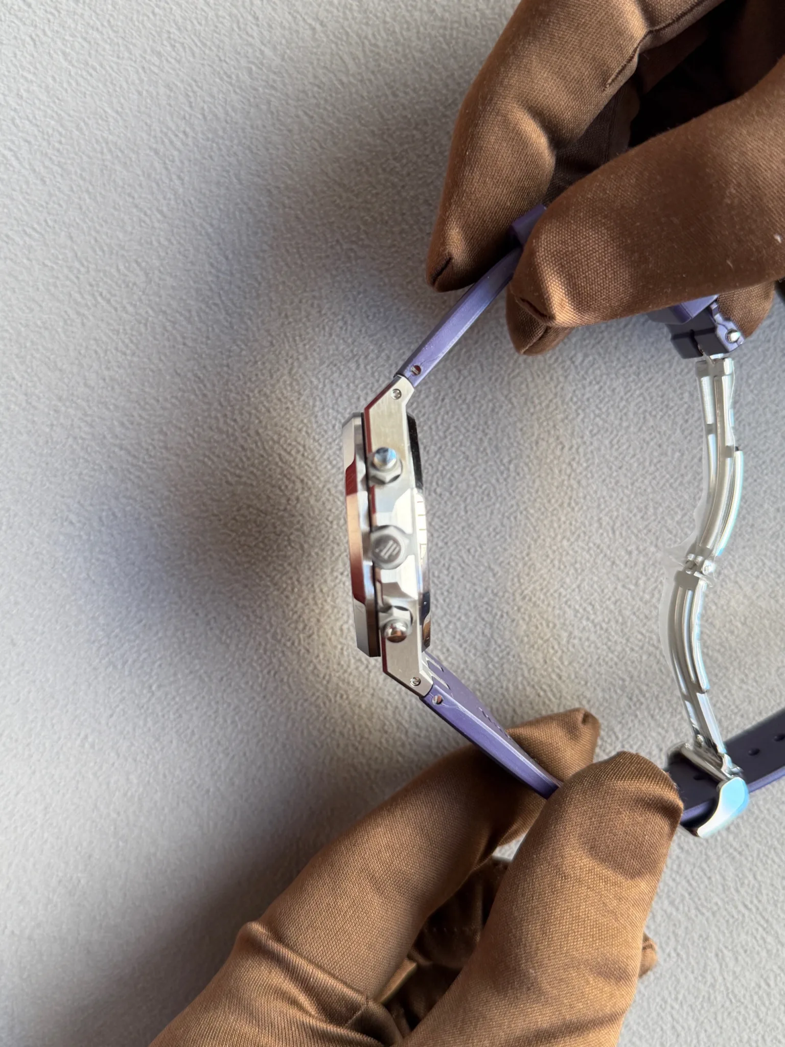 Close-up of gloved hands adjusting a small silver and purple clamp tool against a gray textured background.