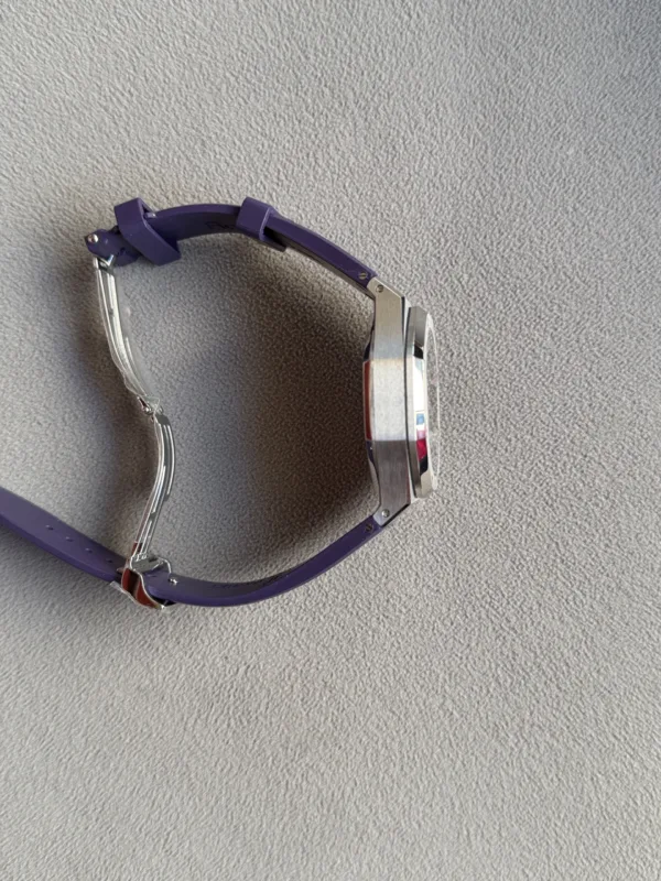 Side view of a silver wristwatch with a purple band on a textured gray background.