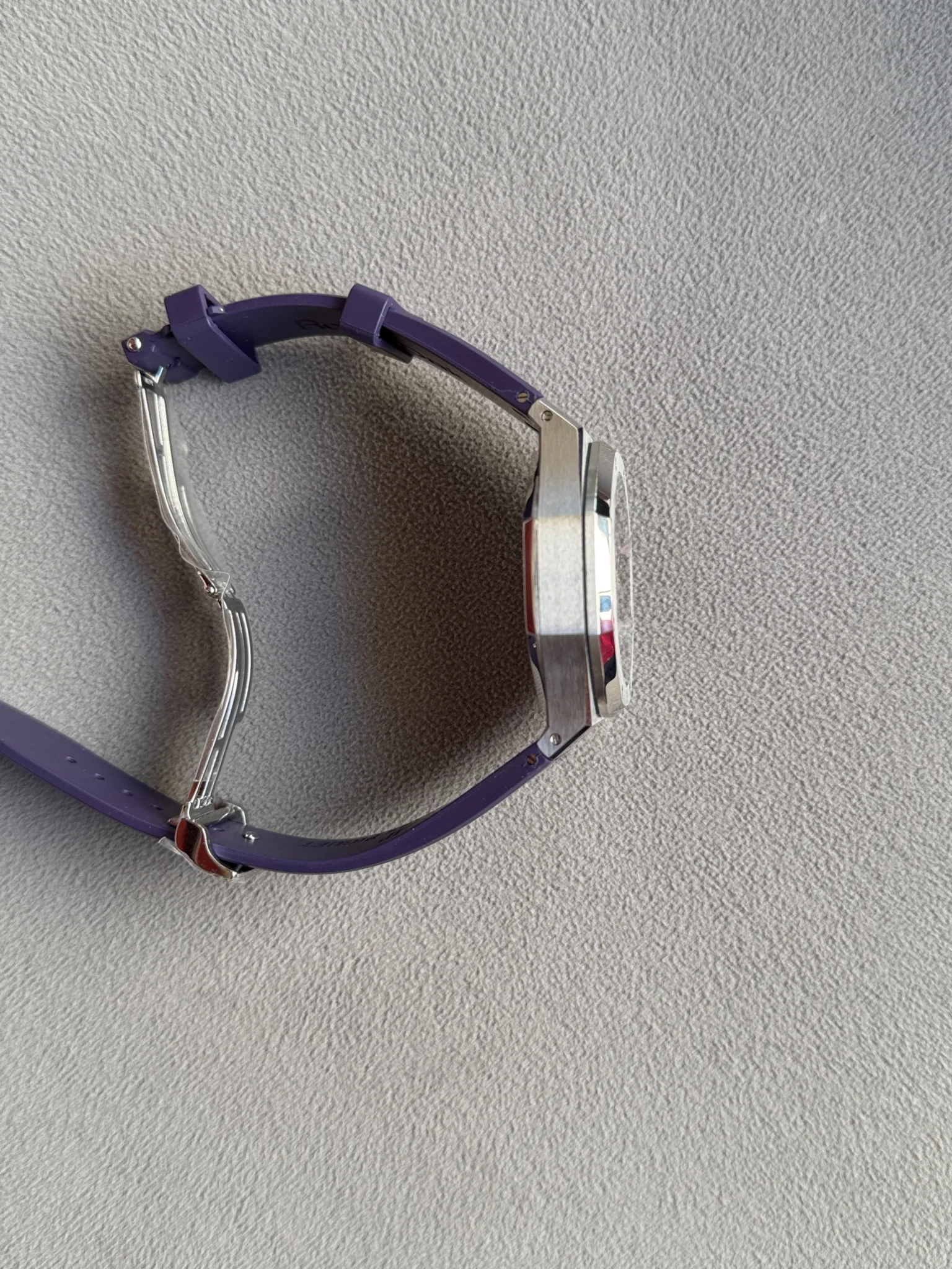 Side view of a silver wristwatch with a purple band on a textured gray background.