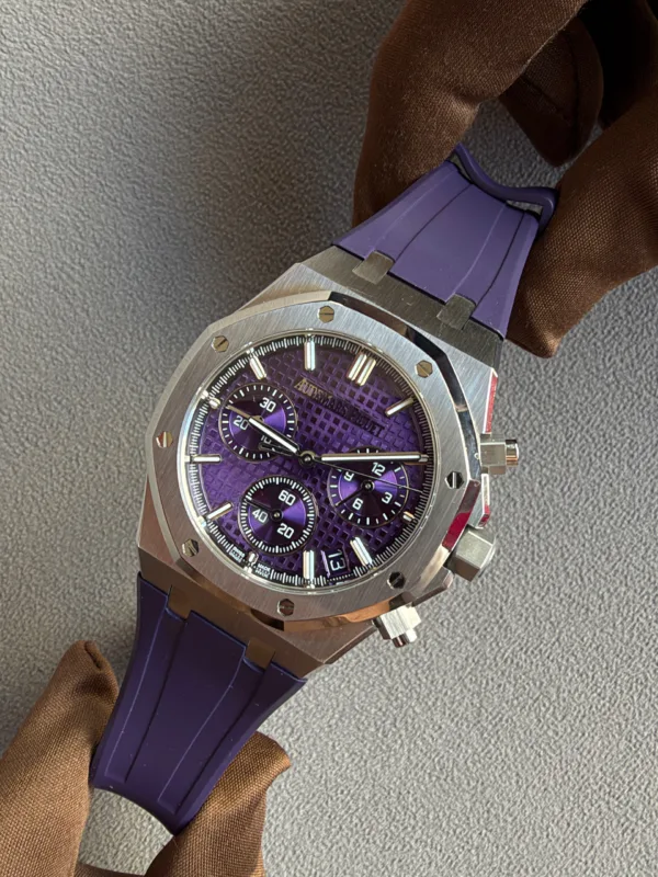Purple-dial wristwatch with a brushed metal case and purple strap resting on a textured gray surface.