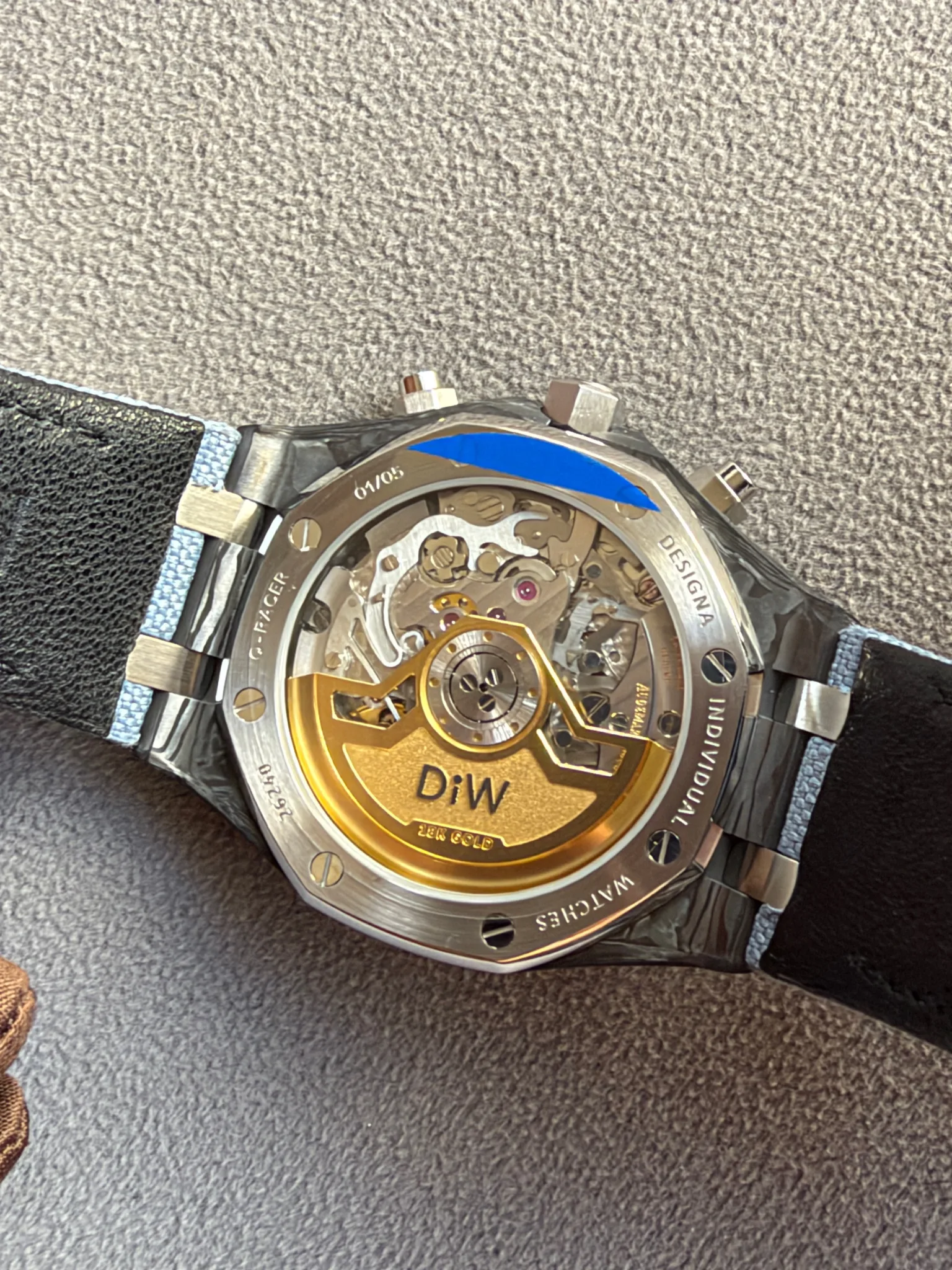 Back of a skeleton wristwatch with visible gears and a gold rotor, metal case and leather strap