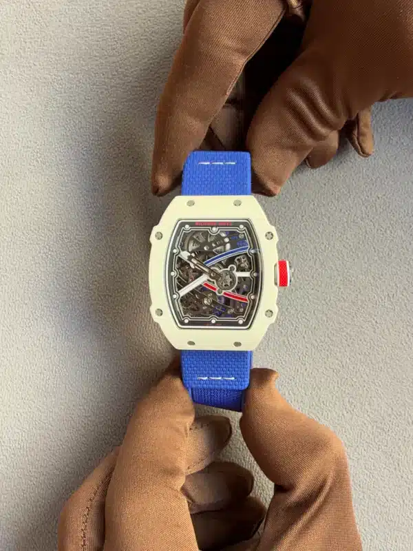 Close-up of a white Richard Mille skeleton watch on a bright blue strap, held by brown gloves, showcasing the intricate inner mechanism through the open dial.