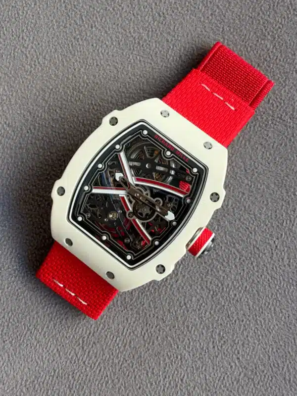 White case skeleton dial watch with a bright red strap on a gray surface, close-up detail shows gears and screws.