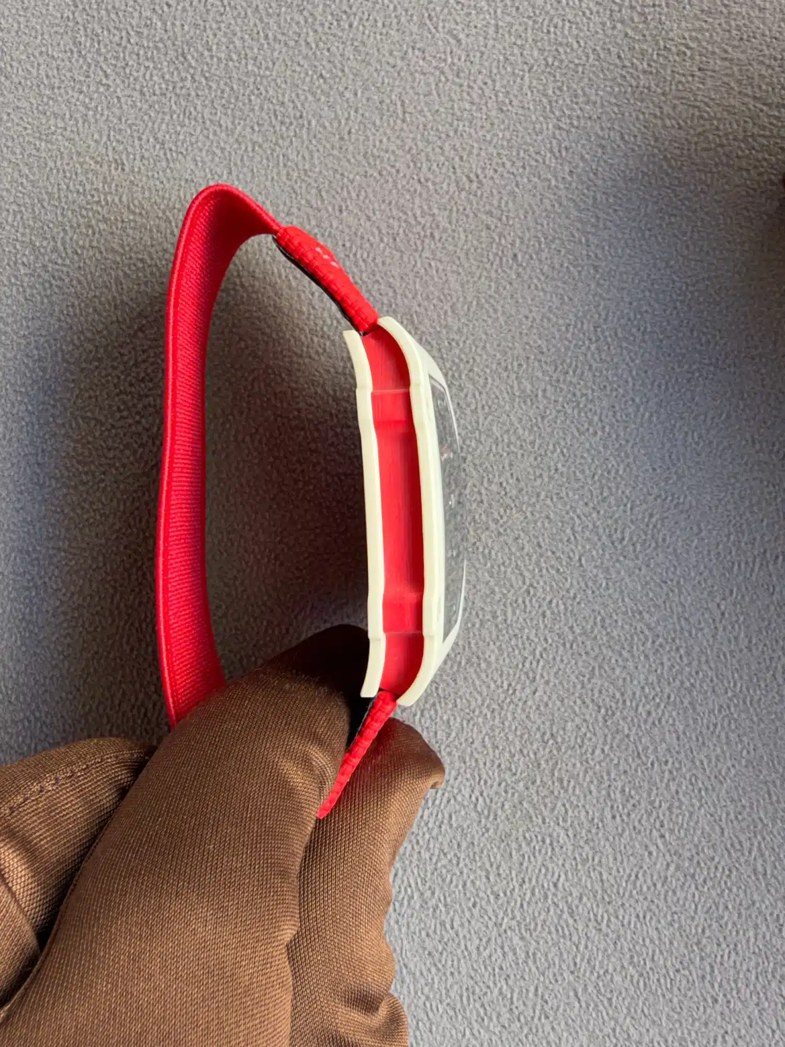 Red over-ear headphones with a white frame resting on a person's brown sleeve, viewed from above on a gray carpet.
