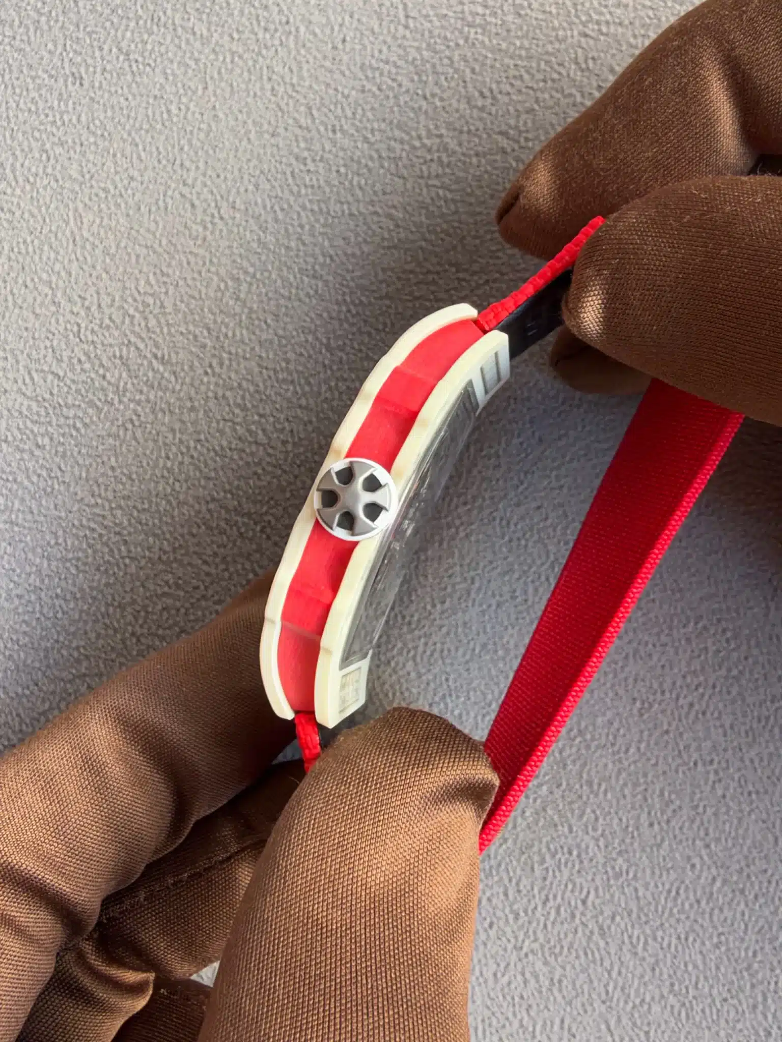 Close-up of a brown-gloved hand threading a red strap through a white plastic buckle with a small gray pulley/guide.