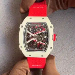 Ticker24Watches - Close-up of a white Richard Mille skeleton watch with a bright red strap being held by gloved hands in a gray background.