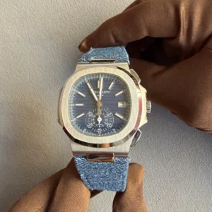 Stainless steel wristwatch with a blue dial and denim strap held by a gloved hand.