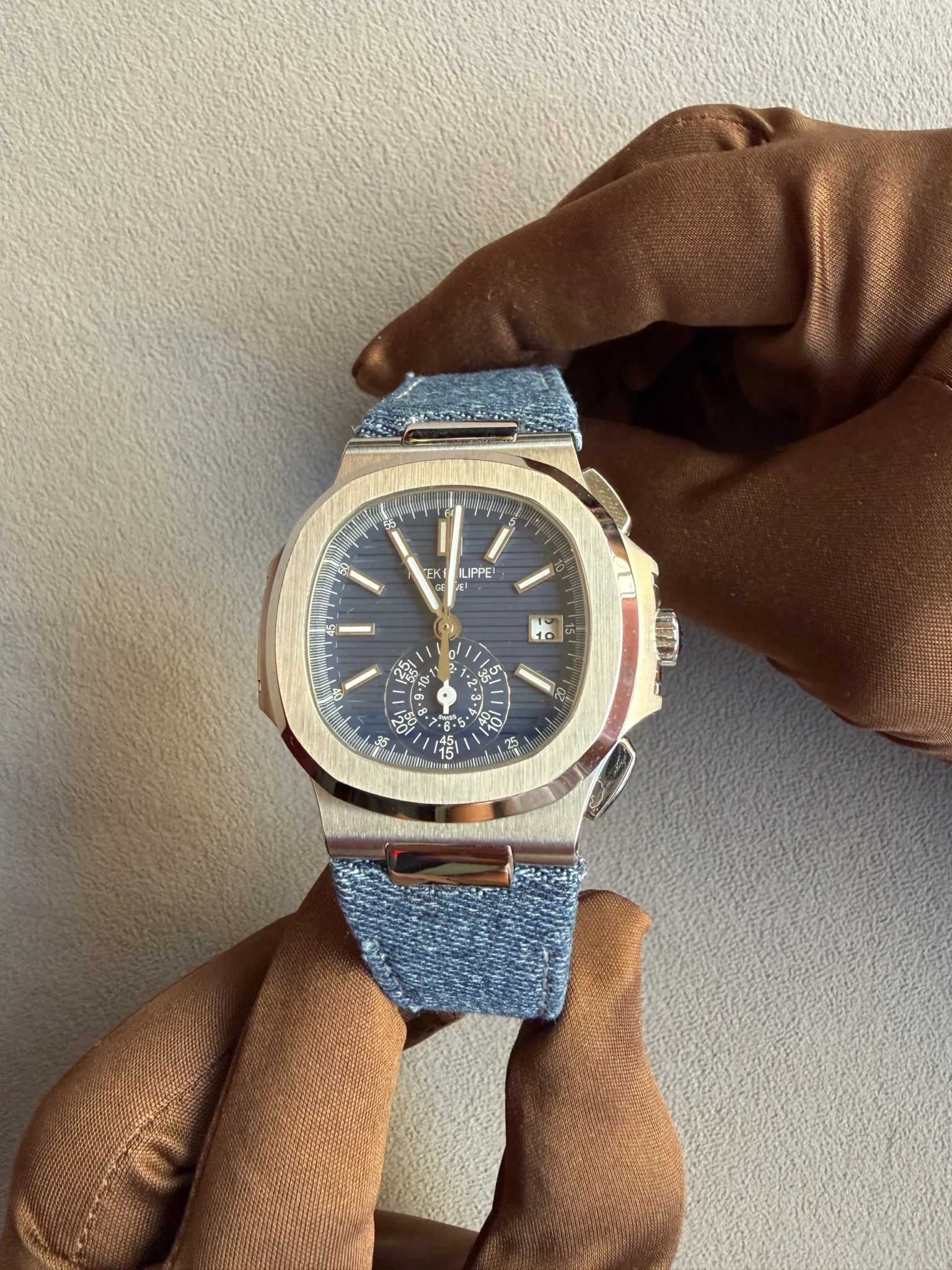 Stainless steel wristwatch with a blue dial and denim strap held by a gloved hand.