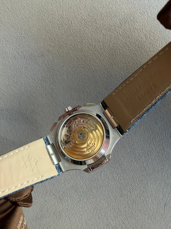Back view of a luxury wristwatch showing its gold rotor and inner movement through a clear case back, brown leather strap visible on the right side.